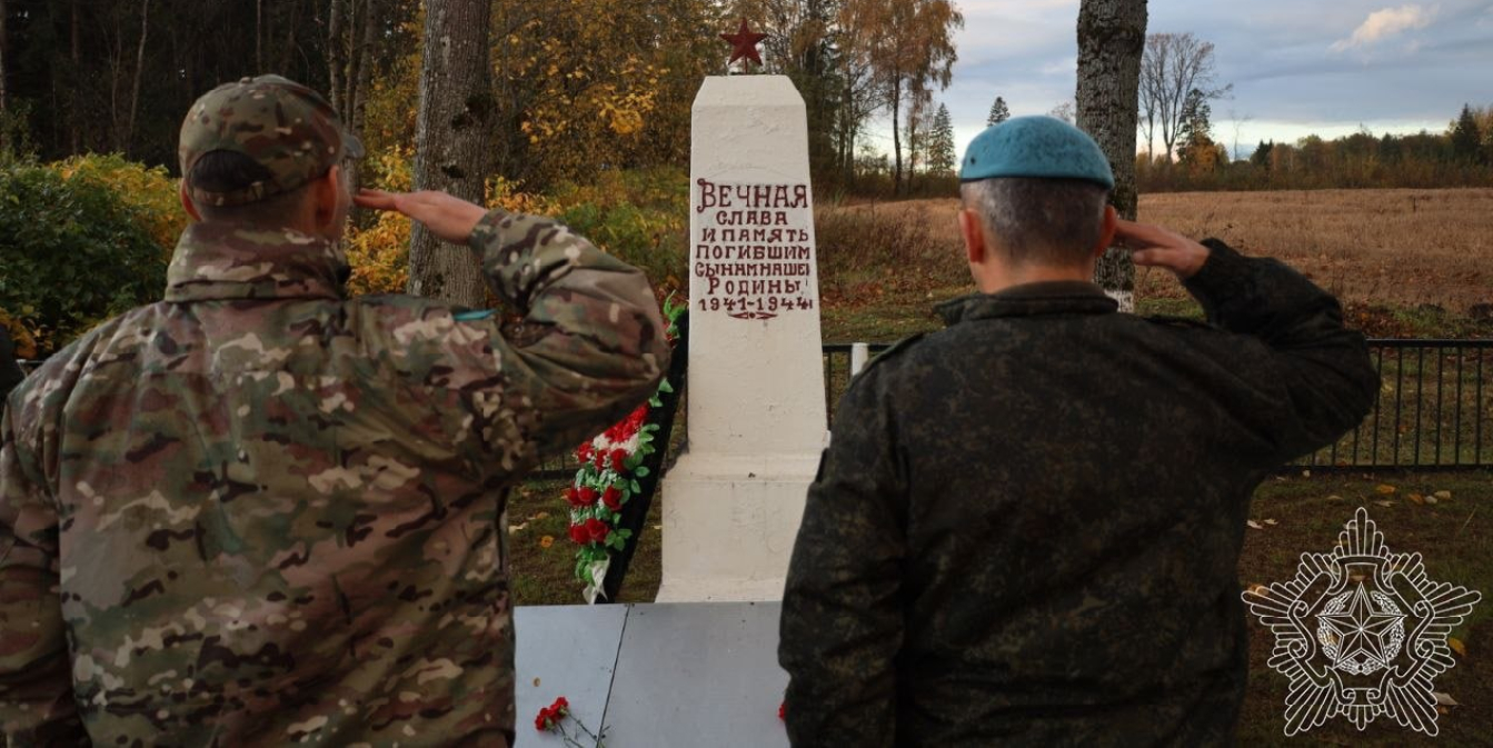 Два военнослужащих со спины отдают воинское приветствие перед памятником советским воинам на братской могиле
